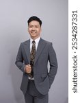 a handsome asian man wearing a suit with a cheerful soul, with a business pose in a gray suit, gray background and natural light in the studio