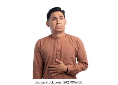 Handsome Asian Muslim man touching his stomach feels hungry and wants to eat delicious food isolated on white background. Ramadan and Eid Fitr celebration concept