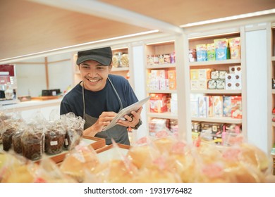 handsome asian smiling worker at the bakery shop checking the product with tablet