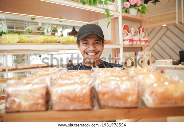 handsome asian smiling worker at the bakery shop\
showing his product