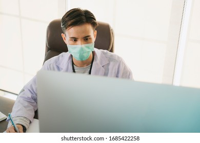 Handsome asian thai doctor wearing mask working in the room at working table. Doctor working on computer researching on vaccine to cure covid-19 virus.