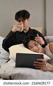 Handsome Asian Young Gay Men Couple Relaxes In The Bedroom, Watching Movie On Tablet Together. A Man Lying On The Pillow On His Boyfriend Lap. Romantic Teenage Gay Couple.