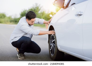 Handsome Asian young man checking wheel flat tire alone on the road. - Powered by Shutterstock