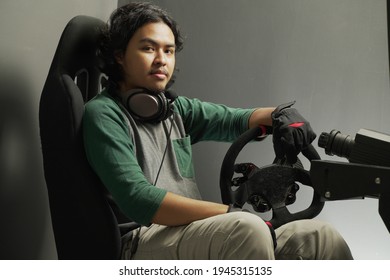 Handsome Asian Young Man Gamer In Headphones With Pc Computer Playing Car Racing Video Game At Home And Steering Wheel