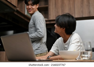 Handsome Asian Young Man Talking With His Boyfriend While He Is Preparing Food In The Kitchen. Happy Gay Couples.