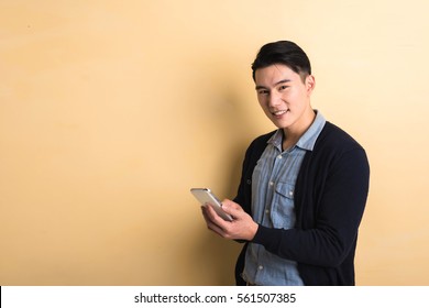 gut aussehender asiatischer junger Mann mit Smartphone, Aufnahme auf Studiogelbem Hintergrund