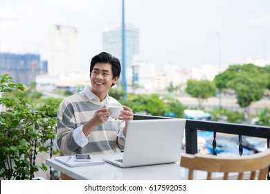 Handsome Asian Young Man Working On Laptop And Smiling While Enjoying Coffee In Cafe