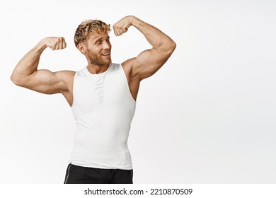 Handsome athlete looking strong, flexing biceps, showing his strong muscles arms, smiling pleased, workout and doing fitness exercises, white background - Powered by Shutterstock