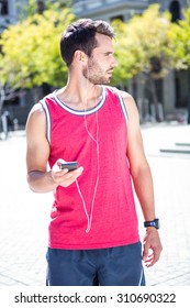 Handsome athlete sending a text while looking away on a sunny day