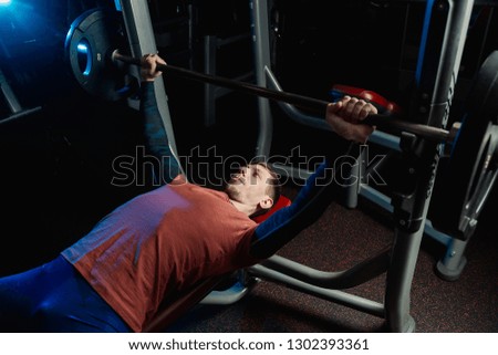 Handsome athletic man performs bench press with a barbell in the gym.