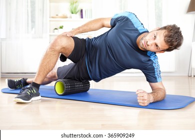 Handsome Athletic Young Man Doing Side Planking with Foam Roller on his Thigh.