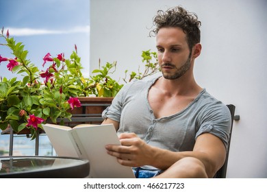 Handsome Athletic Young Man Reading Book Outside Sitting On Terrace In A Summer Day