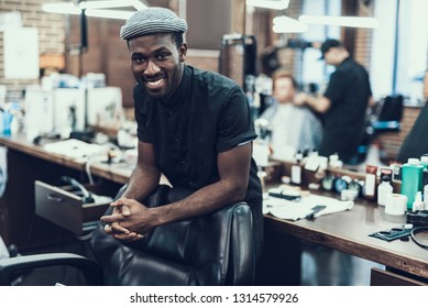 Handsome and attractive barber master looking at camera standing against blurred barbershop