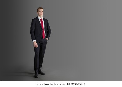 handsome, attractive man in suit and red tie in full length on grey background. confident, serious businessman, lawyer with hand in his pants in pocket. business concept. text