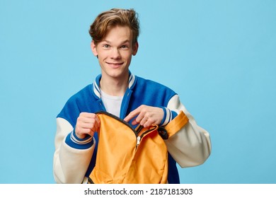 A Handsome, Attractive Young Man With An Orange Backpack In His Hands Stands Smiling Joyfully At The Camera And Points To The Unbuttoned Satchel In His Hands