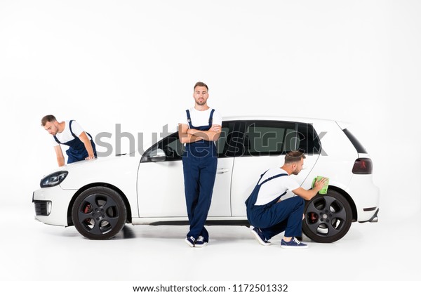 handsome auto mechanic cleaning car and standing\
near car after repairing on\
white