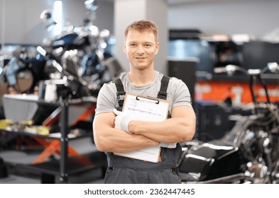 Handsome auto mechanic posing in car service and holding documents in hands. High-quality service of auto technics concept - Powered by Shutterstock