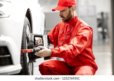 Handsome Auto Mechanic In Red Uniform Fixing Disk For Wheel Alignment At The Car Service