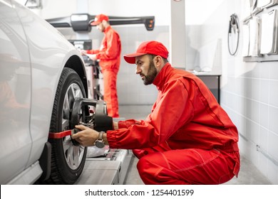 Handsome Auto Mechanic In Red Uniform Fixing Disk For Wheel Alignment At The Car Service