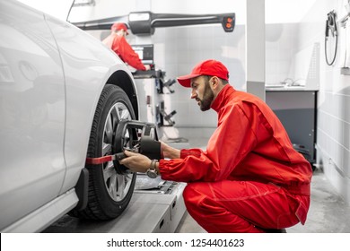 Handsome Auto Mechanic In Red Uniform Fixing Disk For Wheel Alignment At The Car Service