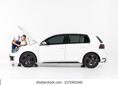 handsome auto mechanic repairing car and looking in open hood on white