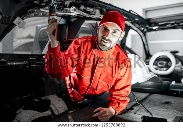 Handsome auto service worker in\
red uniform disassembling new car interior making some\
improvements