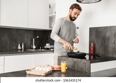 Handsome Bachelor With Short Brown Hair And Beard Cooking Omelet With Vegetables In Home Kitchen Using Frying Pan