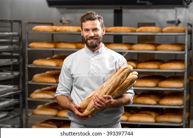 Handsome baker in uniform holding baguettes with bread shelves on the background at the manufacturing - Shutterstock ID 393397744