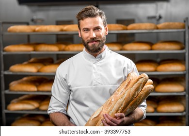 Handsome baker in uniform holding baguettes with bread shelves on the background at the manufacturing - Powered by Shutterstock
