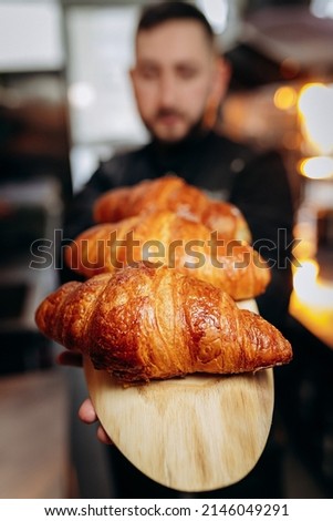 Handsome baker in uniform holding freshly baked croissants at the bakery