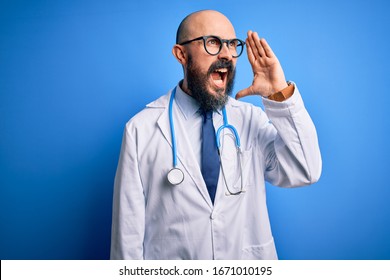 Handsome bald doctor man with beard wearing glasses and stethoscope over blue background shouting and screaming loud to side with hand on mouth. Communication concept.