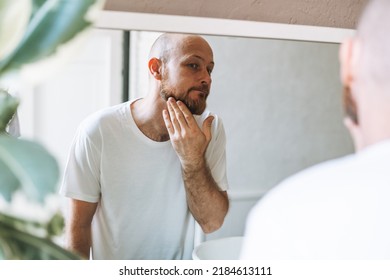 Handsome Bald Man Looking At Mirror And Touching Face In Bathroom