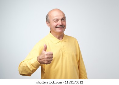 Handsome, Bald Man In Yellow Tshirt With His Thumb Up In Sign Of Optimism Winking On White Background