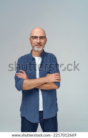 Handsome bald middle aged man in glasses posing with hands folded wearing casual isolated on white background. Senior happy business man in denim jeans and blue shirt. 