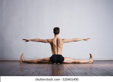 Handsome ballet dancer sitting on a splits. Warm up on the floor.