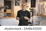 Handsome barista guy work coffee shop. Tattooed hipster man portrait. Happy male face smile. Joy young adult person look camera at cozy cafe house. Stylish dyed hair waiter make hot tasty drink order.