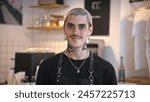 Handsome barista guy work coffee shop. Tattooed hipster man portrait. Happy male face smile. Joy young adult person look camera at cozy cafe house. Stylish dyed hair waiter make hot tasty drink order.