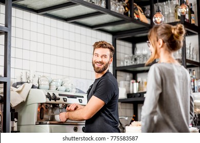 Handsome barista making coffee standing with female client at the bar of the modern cafe interior - Powered by Shutterstock