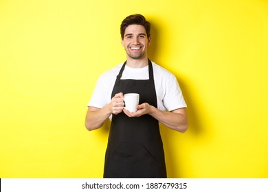 Handsome Barista Serving Coffee, Bring Cup, Standing In Black Apron With Friendly Smile