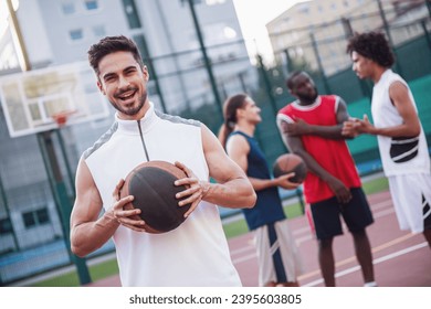 Handsome basketball players are talking and smiling on basketball court outdoors, guy in the foreground is looking at camera - Powered by Shutterstock