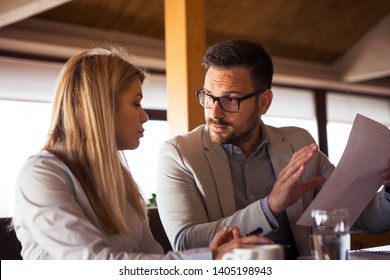 A handsome beard businessman explains to a beautiful colleague what to change in the report while sitting and drinking coffee.