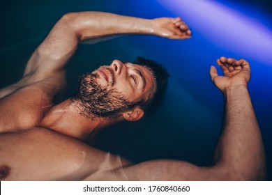 Handsome beard man floating in tank filled with dense salt water used in meditation, therapy, and alternative medicine. 