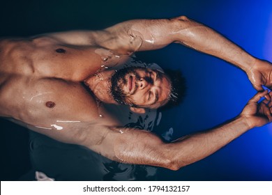 Handsome beard man floating in tank filled with dense salt water used in meditation, therapy, and alternative medicine. 