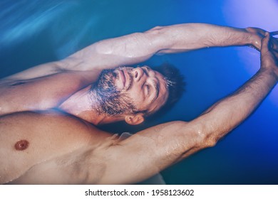 Handsome Beard Man Floating In Tank Filled With Dense Salt Water Used In Meditation, Therapy, And Alternative Medicine. 