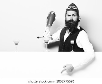 Handsome Bearded Aviator Or Pilot With Long Beard And Mustache On Serious Face With Shaker Alcoholic Cocktail In Vintage Suede Leather Waistcoat With Hand And Glasses On Purple Green Studio Background