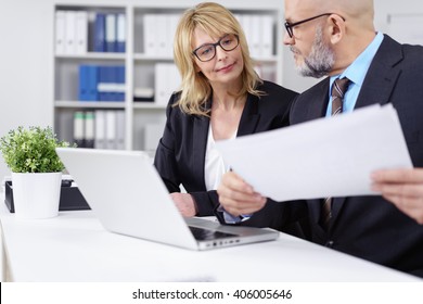 Handsome Bearded Business Man With Necktie, Suit And Eyeglasses Showing Woman Something On Papers Next To Computer