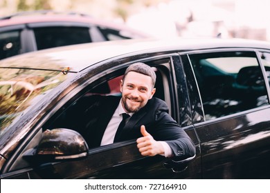 Handsome bearded businessman in a car with thumbs up