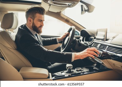 Handsome bearded businessman is sitting in a new car in car dealership