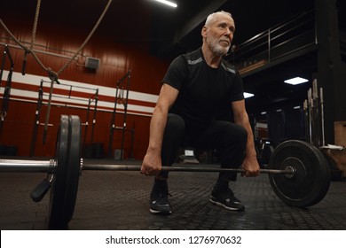 Handsome bearded Caucasian male pensioner with strong muscled arms holding barbell, ready to do deadlift. Self determined elderly man in sportswear working on stamina and building muscles in gym - Powered by Shutterstock