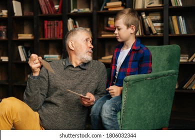 Handsome bearded gray-haired grandfather with his cute grandson having fun looking at an old photo album, enjoying memories watching family photo album at home in living room background on bookshelves - Powered by Shutterstock